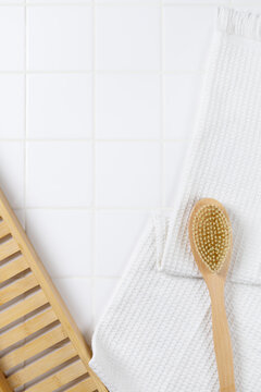Top view of bathroom product mockup background with copy space. Flat lay of body brush, bath puff, and white towel on square tile wall for cosmetic display.
