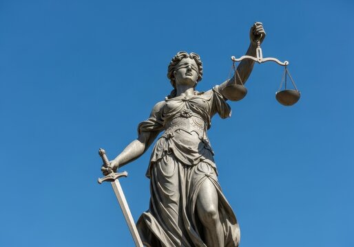 Statue of lady justice holding scales and sword against a clear blue sky