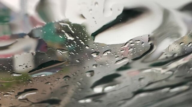 View through a rain-soaked car windshield during a downpour, with blurred traffic and water droplets creating a moody driving scene and reduced visibility