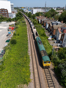 Aerial view of a freight train moving along tracks through a suburban neighborhood with residential houses and green vegetation in London Borough of Ealing, England, United Kingdom.