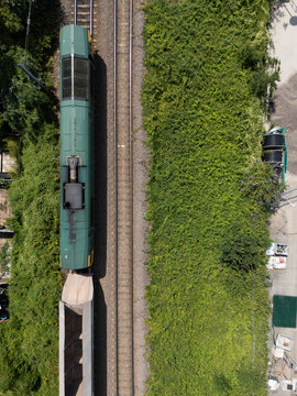 Aerial view of a freight train moving along railway tracks surrounded by lush green vegetation and trees in London Borough of Ealing, England, United Kingdom.