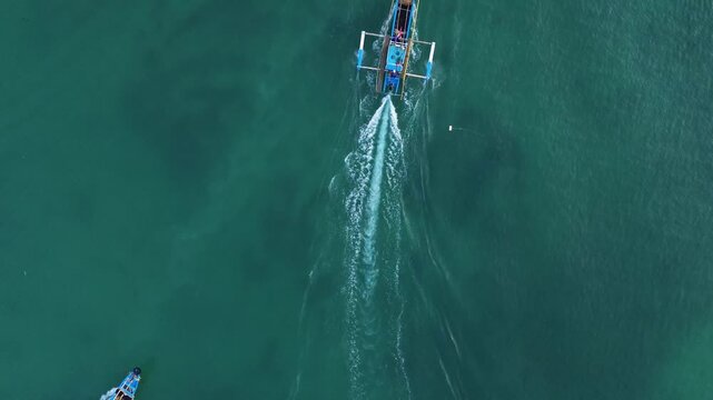 Aerial drone footage of a traditional fishing boat sailing across the vast open ocean. Cinematic aerial perspective capturing the vessel moving through deep blue waters with gentle waves