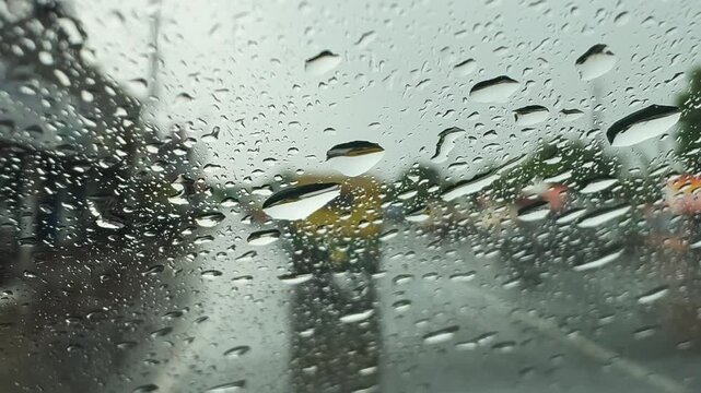 View through a rain-soaked car windshield during a downpour, with blurred traffic and water droplets creating a moody driving scene and reduced visibility