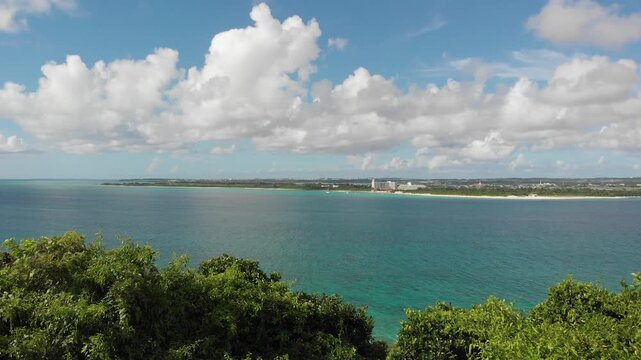 Drone aerial view rising over lush green trees revealing beautiful tropical ocean and resort coast