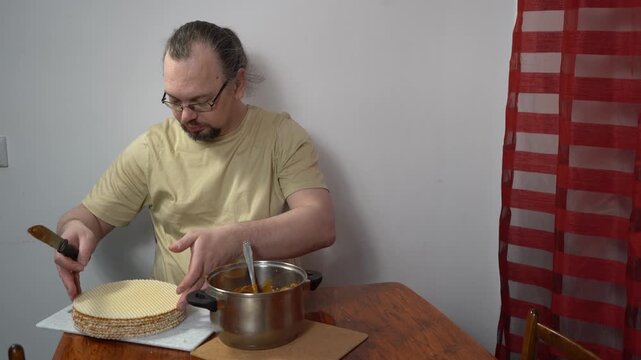 Spread cream on the cakes. Man is making a waffle cake with condensed milk. Sweet food at home.