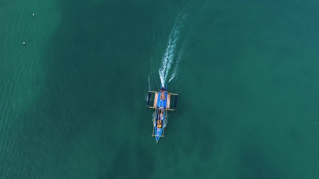 Aerial drone footage of a traditional fishing boat sailing across the vast open ocean. Cinematic aerial perspective capturing the vessel moving through deep blue waters with gentle waves