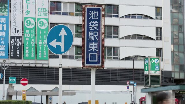 Tokyo Scene  :  Name Sign of Ikebukuro Station, Located in One of Tokyo's Leading Shopping Districts, with People Crossing the Street  |  Ikebukuro, Tokyo, Japan