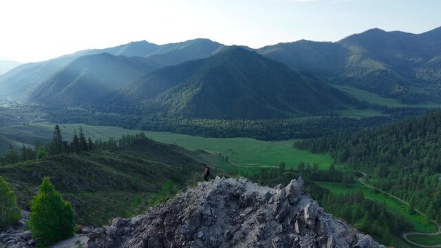 Low angle drone tracking shot of an athletic male tourist stepping down from a steep rocky ledge at Chike-Taman Pass in Altai.