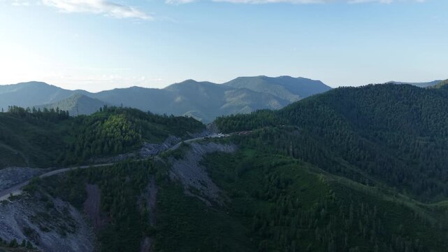 Cinematic drone flight moving forward towards a narrow rocky road cleft surrounded by green larch trees at Chike-Taman Pass in Altai.