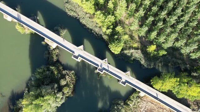 A top-down aerial view of a rural bridge crossing a calm green river surrounded by dense trees along the Camino de Santiago in northern Spain