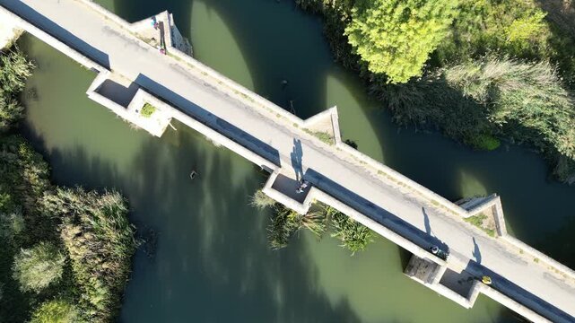 A top-down aerial view of a rural bridge spanning a calm river, captured in a soft, blurred style along the Camino de Santiago in Spain
