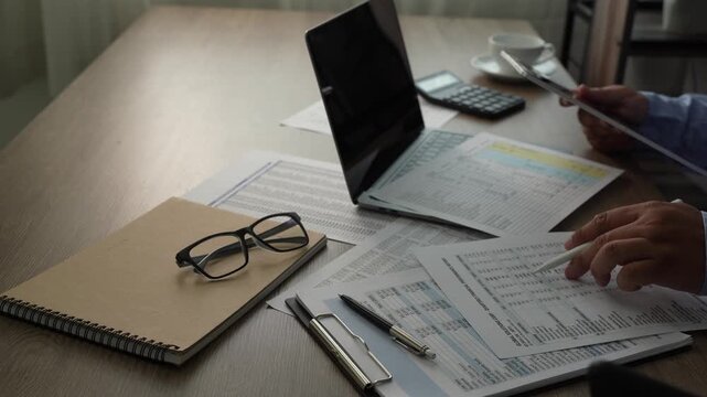 man presses a calculator over accounting reports beside a laptop, reviewing financial figures with a pen on a desk for report preparation, bookkeeping tasks, and business finance content.