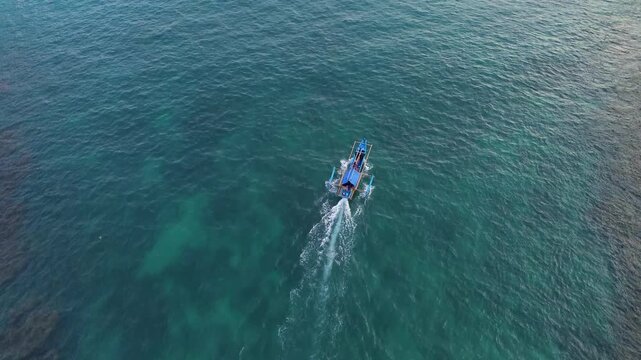 Aerial drone footage of a traditional fishing boat sailing across the vast open ocean. Cinematic aerial perspective capturing the vessel moving through deep blue waters with gentle waves