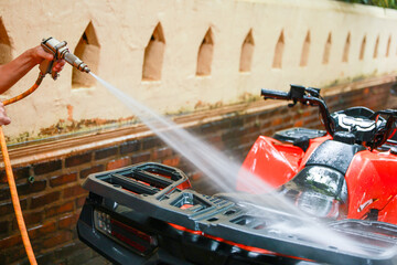 Naklejka premium Person hand water spray cleaning red ATV outdoor wall brick vehicle washing transportation maintenance summer wet hose pressure equipment fresh shine detail care dirt splash garden powerful stream
