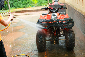 Washing cleaning red ATV outdoor water spray hose vehicle maintenance driveway wet summer transportation recreation four wheeler dirt mud cleaning process person hand garden backyard power washing © CoreRock