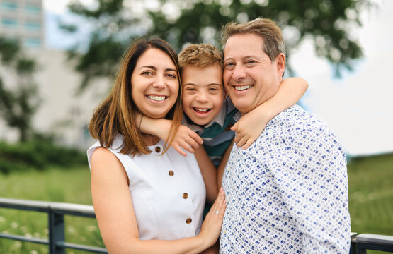 cute little child with trisomy 21 syndrome outside in summer season with his family mother and father