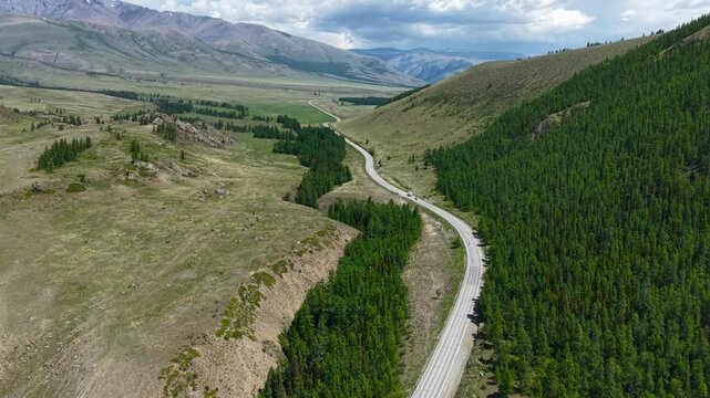 High-angle drone aerial view flying forward over a scenic asphalt highway winding through a lush green valley in Altai.