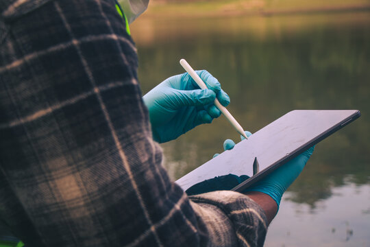 Environmental researchers collecting freshwater samples to monitor pollution and save the information on the tablet.