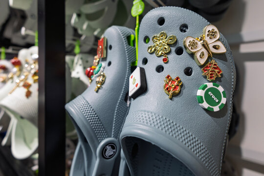 Singapore - January 21, 2026: A close-up view of a slate blue Crocs foam clog personalized with elegant Chinese New Year festive icons and a casino themed Jibbitz shoe charm on a retail hanger.