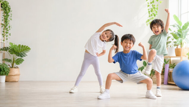 Happy children exercising together indoors, stretching and posing playfully in bright room with green plants and wooden floor