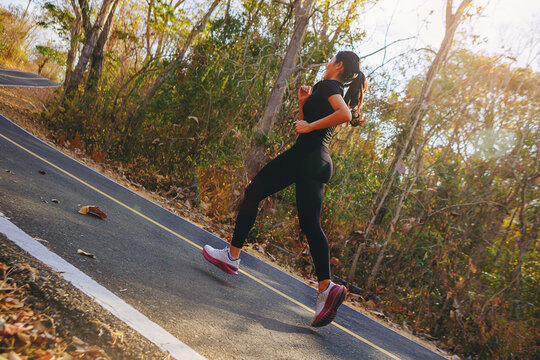 Silhouette of young woman running sprinting on road. Fit runner fitness runner during outdoor workout with sunset background
