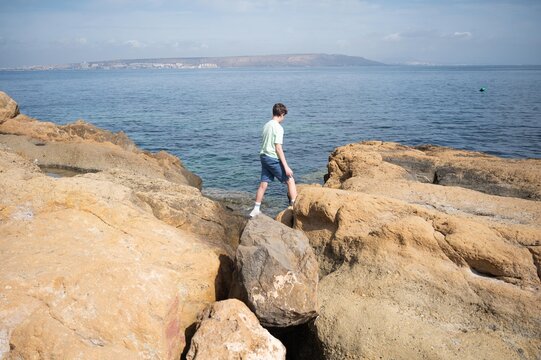 Teenage boy exploring the rocky coastline of Tabarca on a sunny summer morning during a family vacation by the Mediterranean Sea