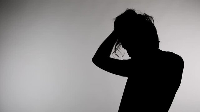 An anonymous silhouette of a man stands against a white background, holding his head with his hands and raising his hair