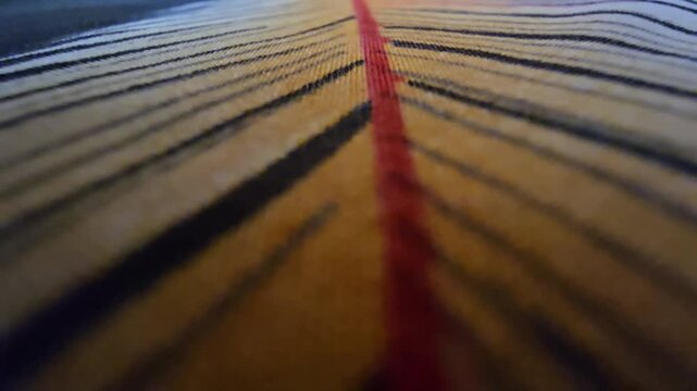 Macro close-up of a textured fabric with parallel mustard yellow, black, and white striped pattern and a bold central red line, high-quality textile background, abstract artistic woven material detail