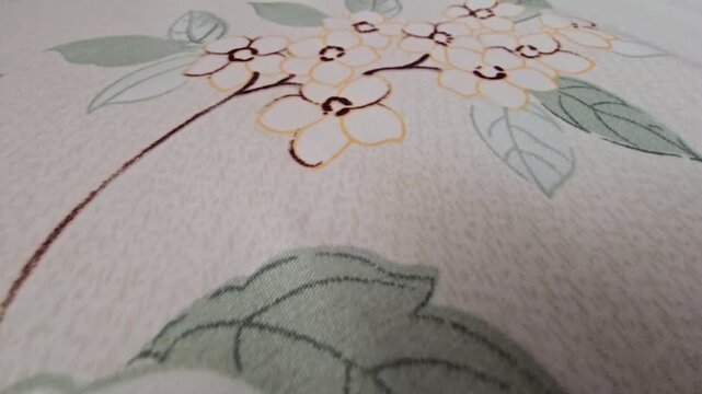 Close-up of a delicate white flower pattern with soft green leaves printed on a textured fabric surface, ideal for textile design, interior decoration, and artistic wallpaper backgrounds, elegant bota