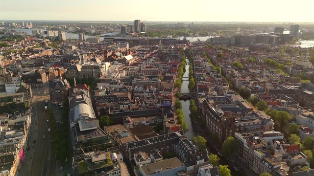 Aerial drone flies forward above Amsterdam aligned with a canal on the right side revealing the historic center and IJ