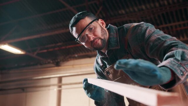 Carpenter, man and blow dust with plank in workshop, furniture manufacturing or production process. Woodwork, person and remove sawdust, craftsmanship and wipe shavings to clean in carpentry industry