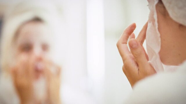 A woman applies a soothing aloe vera face mask in a bright bathroom, immersing her skin in deep hydration. The skincare routine uses a fabric moisturizer sheet, highlighting modern home pampering