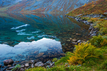 Obraz premium Mountain scenery in Innerdalen, Norway during autumn shows reflections on calm water at the edge of a rocky shore