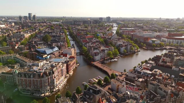 Drone orbits above Amsterdam city center revealing the Amstel River scenic canal intersections and historic bridges
