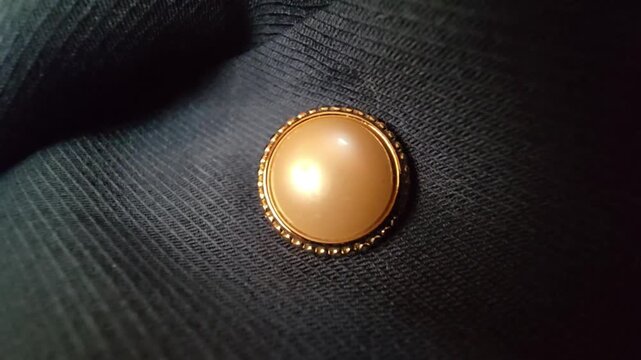 Elegant macro close-up of a luxurious cream pearl button with a decorative gold frame, set against a dark textured fabric background, ideal for fashion design, formal wear, and high-end clothing detai