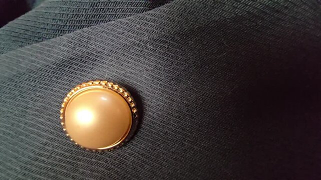 Elegant macro close-up of a luxurious cream pearl button with a decorative gold frame, set against a dark textured fabric background, ideal for fashion design, formal wear, and high-end clothing detai