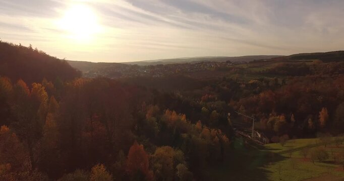 Aerial view soaring above a rocky stone ridge surrounded by dense colorful autumn tree forest