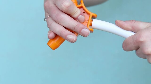 Preparing PEX pipe with orange three-sided chamfering tool. Using hand calibrator to prepare metal-plastic pipe for installation. Close-up of hands while working. Plumbing work