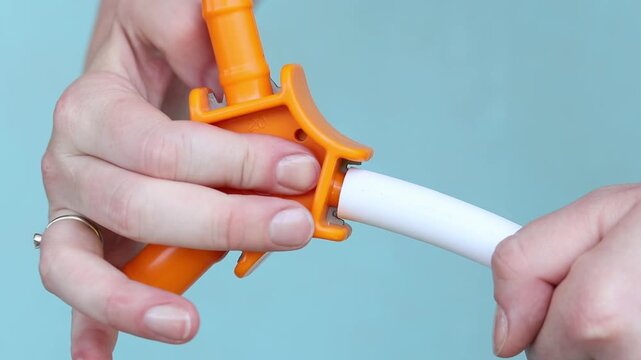 Process of calibrating plastic pipe with orange hand tool. Using hand calibrator to prepare metal-plastic pipe for installation. Close-up of hands while working. Plumbing work