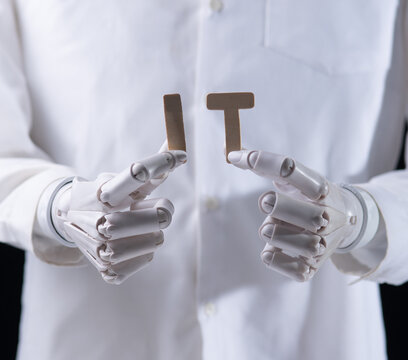 Robot hands holding wooden letters forming word IT on dark background.