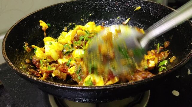 Close up of boiled egg pieces being stirred with rich Indian onion masala, spices and fresh coriander in a traditional kadhai or pan during home cooking.