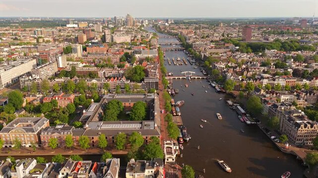 Drone orbits above Amsterdam canal district revealing the Amstel river lined with historic town buildings and boats