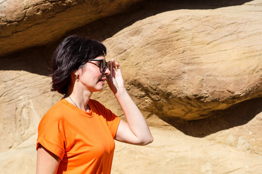 Young woman in a short summer orange dress and sunglasses enjoying sunny day outdoors, radiating joy and vibrant summer vibes.