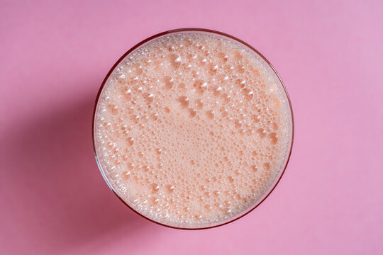 Fresh strawberry smoothie or milkshake with bubbles in glass on pink background, top view. Minimalist flat lay for cafe menu morning routine beverage catering or summer sweet dessert promotion
