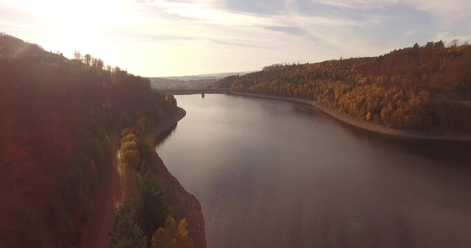 Drone flight over a large lake reservoir with autumn colored forests stretching to the horizon