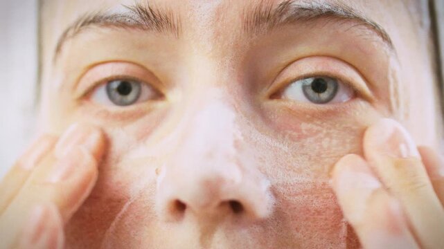 Girl gently washes her facial skin with white cleansing foam in bright bathroom. The soft foam lifts makeup and impurities, highlighting a daily skincare ritual that leaves her skin fresh and radiant