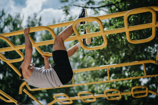 Young man hangs from yellow monkey bars performing a bodyweight exercise in an outdoor park. The athlete trains on playground bars, demonstrating strength and balance during a casual workout.