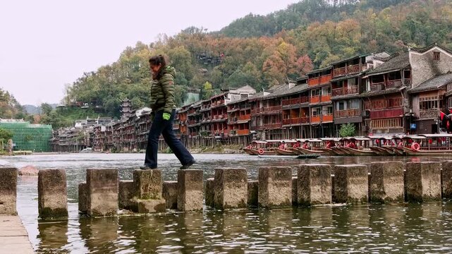 Female tourist walking on stepping stones in Fenghuang Ancient Town, China
