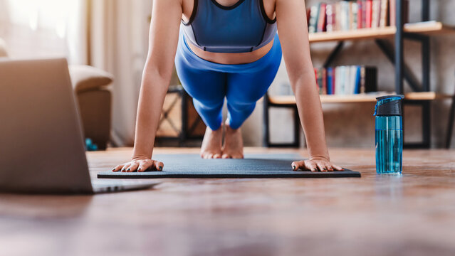 Cropped shot of young woman watching training videos on laptop while exercising at home, fit female doing online workout, fitness and healthy lifestyle concept