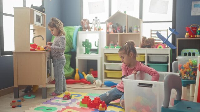 Girl plays with colorful blocks and toy kitchen using hands while kneeling on foam mat in a bright indoor playroom; quiet concentration.